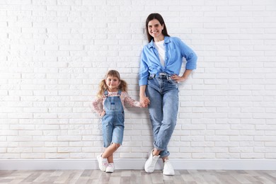 Photo of Beautiful mother and her little daughter near white brick wall