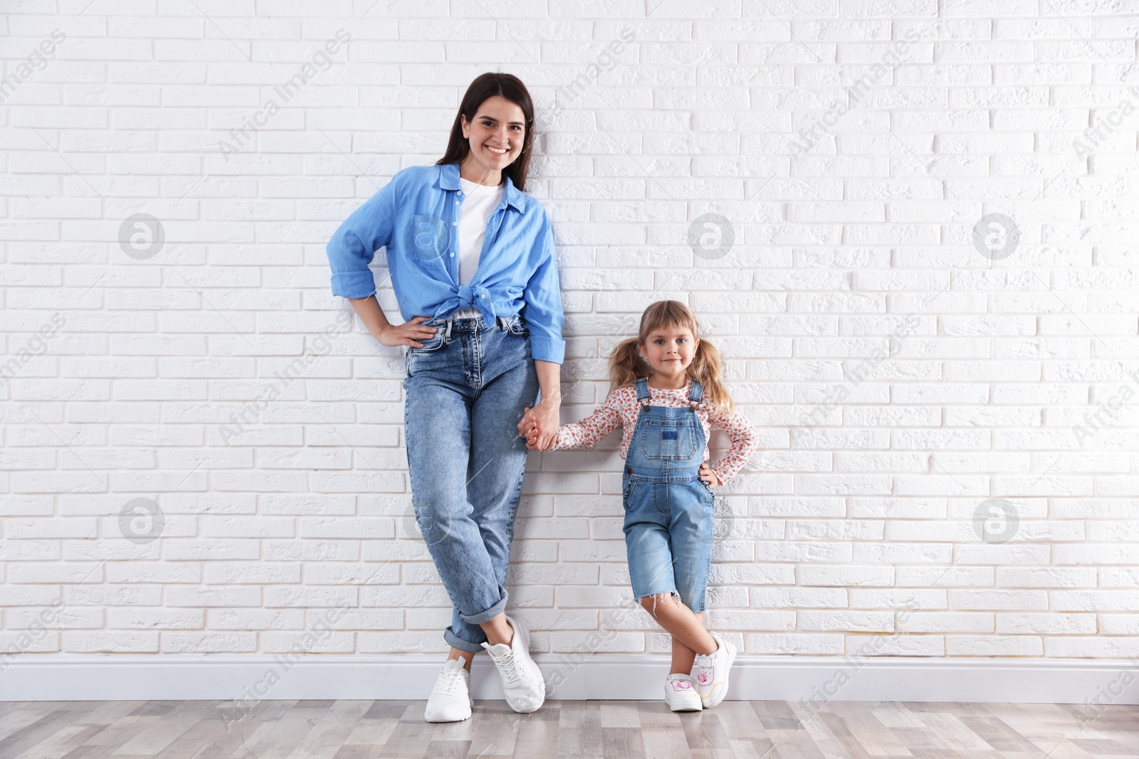 Beautiful mother and her little daughter near white brick wall Photo of Beautiful mother and her little daughter near white brick wall