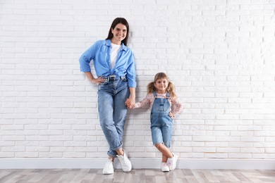 Photo of Beautiful mother and her little daughter near white brick wall