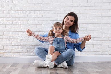Photo of Beautiful mother and her little daughter near white brick wall
