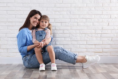 Photo of Beautiful mother and her little daughter near white brick wall. Space for text
