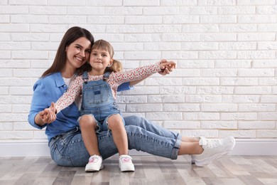 Photo of Beautiful mother and her little daughter near white brick wall. Space for text
