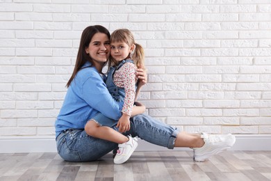 Photo of Beautiful mother and her little daughter near white brick wall. Space for text