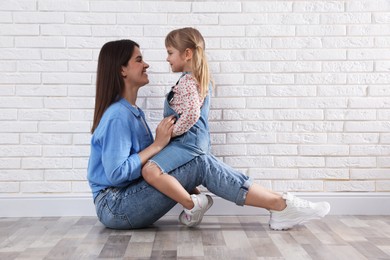 Photo of Beautiful mother and her little daughter near white brick wall. Space for text