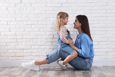 Photo of Beautiful mother and her little daughter near white brick wall. Space for text