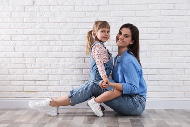 Photo of Beautiful mother and her little daughter near white brick wall. Space for text