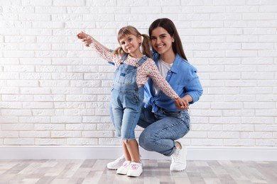 Photo of Beautiful mother and her little daughter near white brick wall