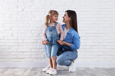 Photo of Beautiful mother and her little daughter near white brick wall