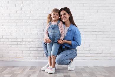 Photo of Beautiful mother and her little daughter near white brick wall