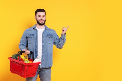 Photo of Man with shopping basket full of products pointing at something orange background, space for text