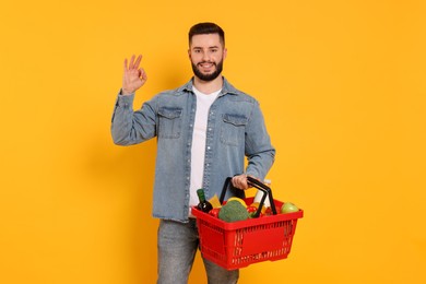 Photo of Man with shopping basket full of products showing ok gesture on orange background