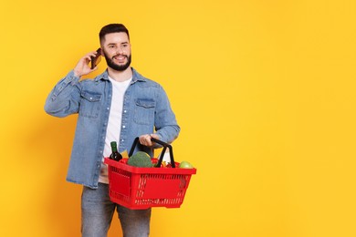 Photo of Man with shopping basket full of products talking on smartphone against orange background, space for text
