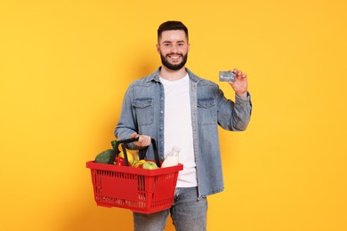 Photo of Man with shopping basket full of products and credit card on orange background