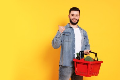Photo of Man with shopping basket full of products pointing at something orange background, space for text