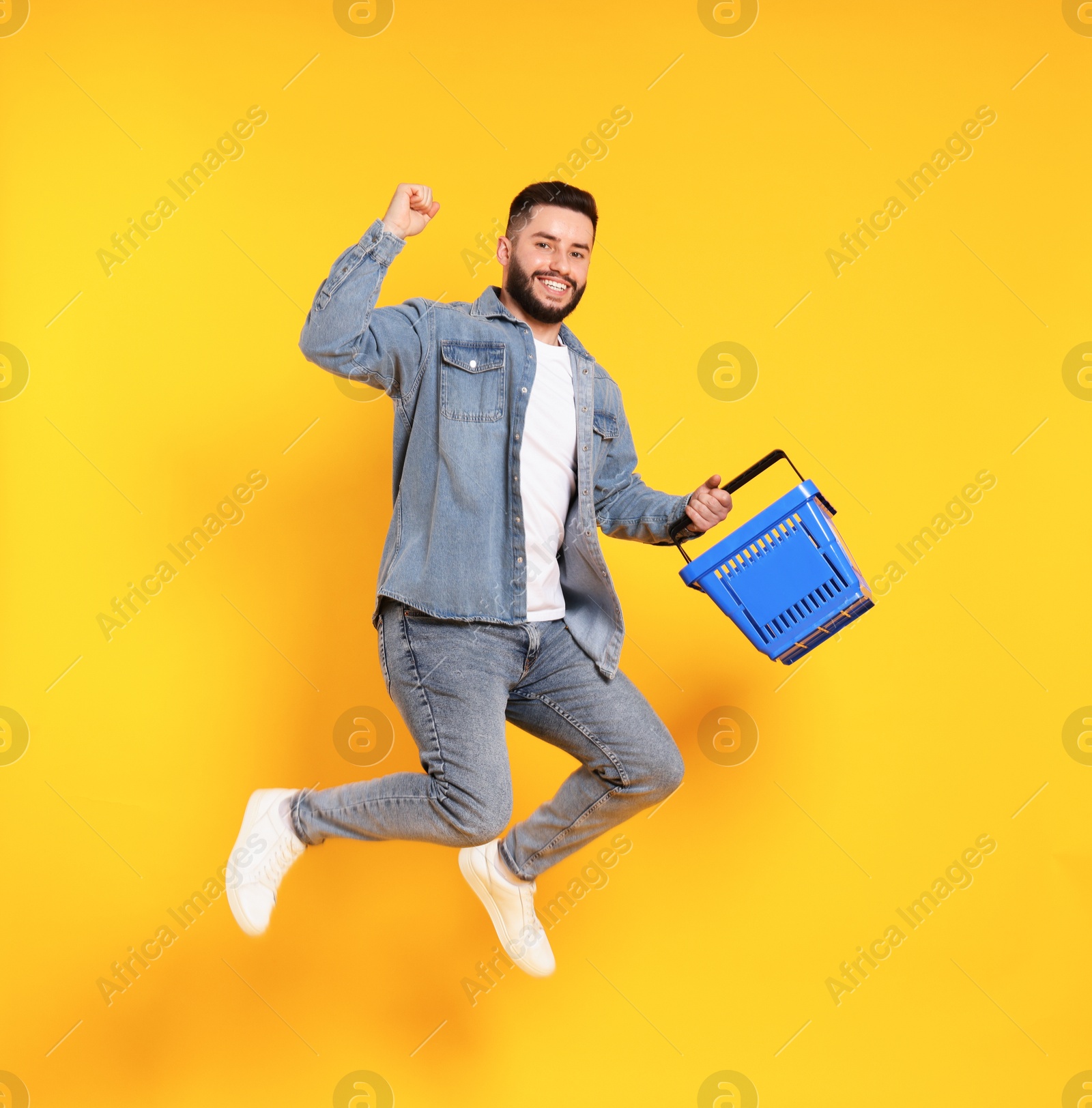 Man with empty shopping basket jumping on orange background Photo of Man with empty shopping basket jumping on orange background