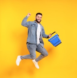 Photo of Man with empty shopping basket jumping on orange background