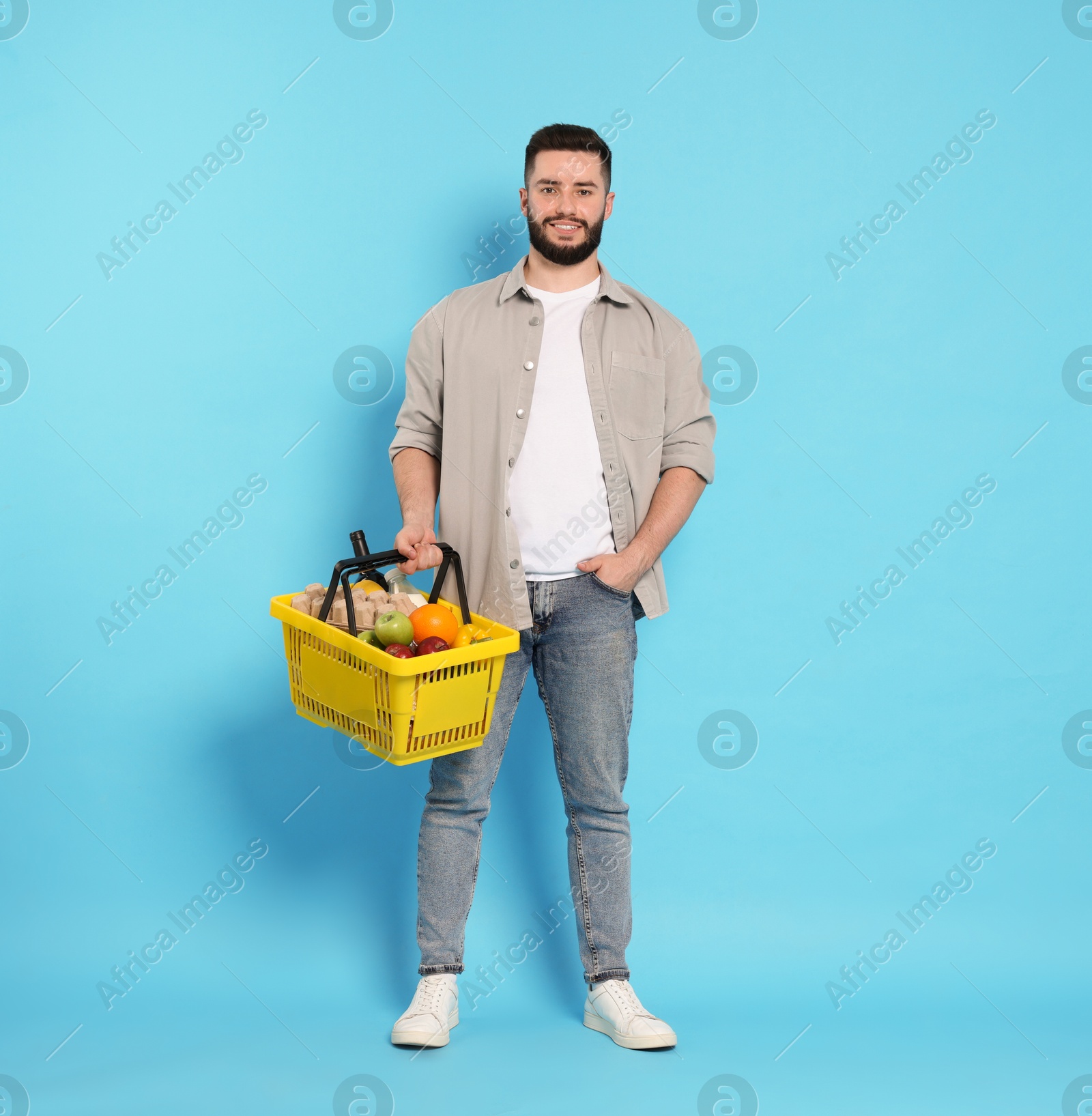 Man with shopping basket full of products on light blue background Photo of Man with shopping basket full of products on light blue background