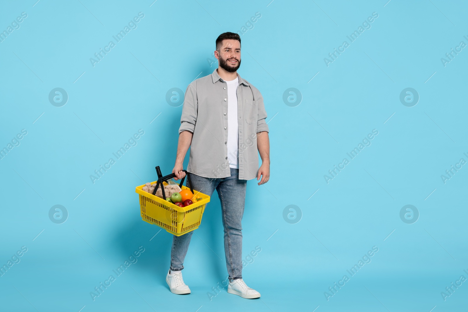 Man with shopping basket full of products on light blue background Photo of Man with shopping basket full of products on light blue background