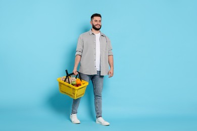Photo of Man with shopping basket full of products on light blue background