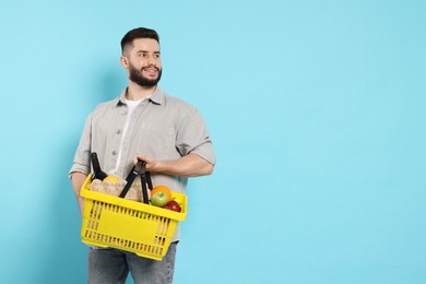 Photo of Man with shopping basket full of products on light blue background, space for text