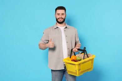 Photo of Man with shopping basket full of products showing thumbs up on light blue background