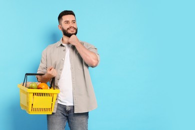 Photo of Man with shopping basket full of products on light blue background, space for text