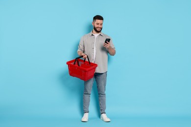 Photo of Man with empty shopping basket and smartphone on light blue background