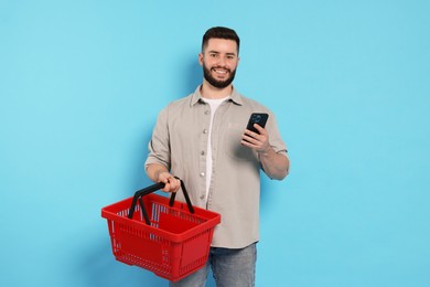 Photo of Man with empty shopping basket and smartphone on light blue background