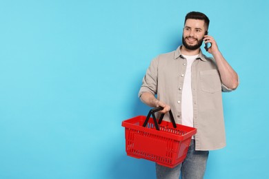 Photo of Man with empty shopping basket talking on smartphone against light blue background, space for text