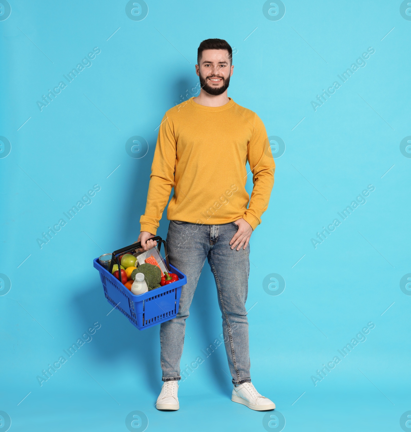 Man with shopping basket full of products on light blue background Photo of Man with shopping basket full of products on light blue background