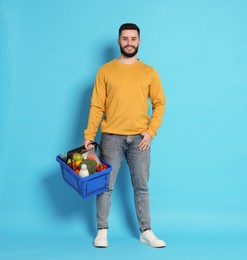 Photo of Man with shopping basket full of products on light blue background