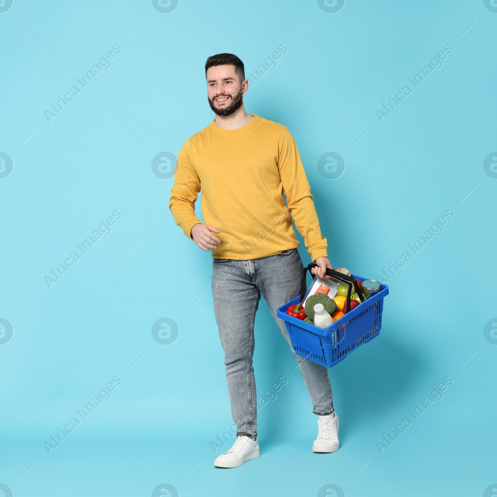 Man with shopping basket full of products on light blue background Photo of Man with shopping basket full of products on light blue background