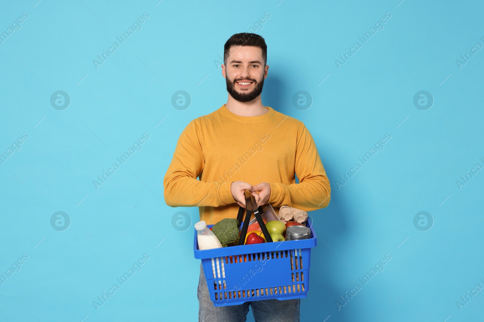 Man with shopping basket full of products on light blue background Photo of Man with shopping basket full of products on light blue background