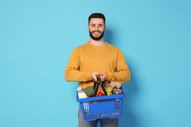 Photo of Man with shopping basket full of products on light blue background