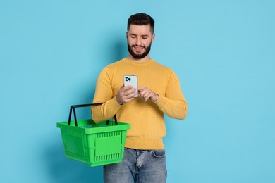 Photo of Man with empty shopping basket and smartphone on light blue background
