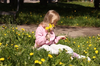 Photo of Cute little girl picking beautiful dandelions in park