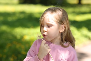 Photo of Cute little girl blowing beautiful dandelion outdoors, space for text