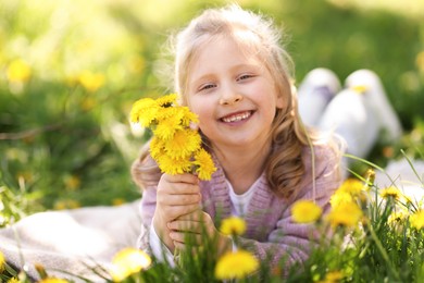 Photo of Cute little girl with beautiful dandelions on green grass outdoors, space for text