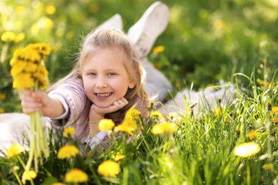 Photo of Cute little girl with beautiful dandelions on green grass outdoors, space for text