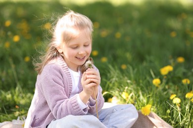 Photo of Cute little girl with beautiful dandelion on green grass outdoors, space for text