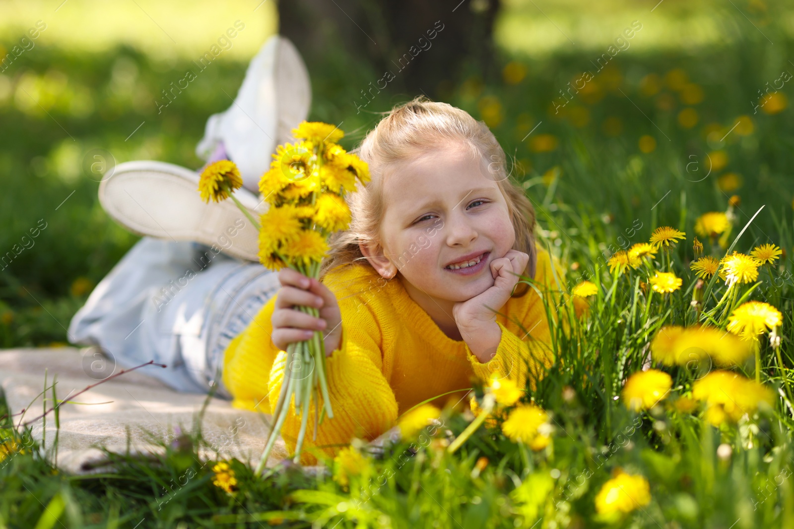 Cute little girl with beautiful dandelions on green grass outdoors Photo of Cute little girl with beautiful dandelions on green grass outdoors