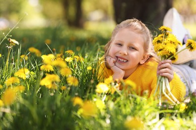 Photo of Cute little girl with beautiful dandelions on green grass outdoors