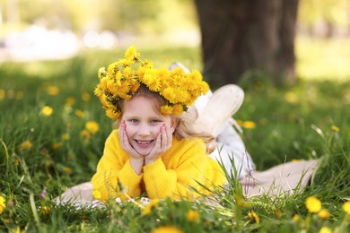 Photo of Cute little girl wearing wreath of dandelions on green grass in park