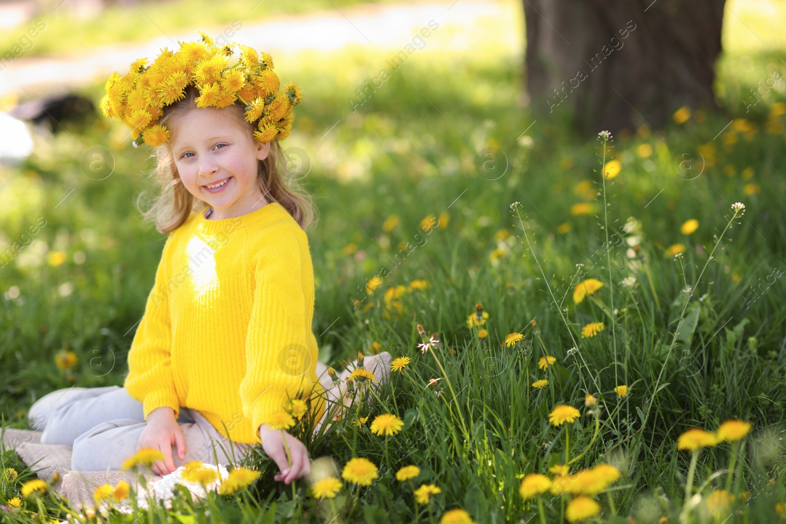 Cute little girl wearing wreath of dandelions on green grass in park Photo of Cute little girl wearing wreath of dandelions on green grass in park