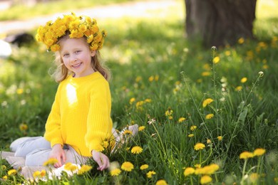 Photo of Cute little girl wearing wreath of dandelions on green grass in park