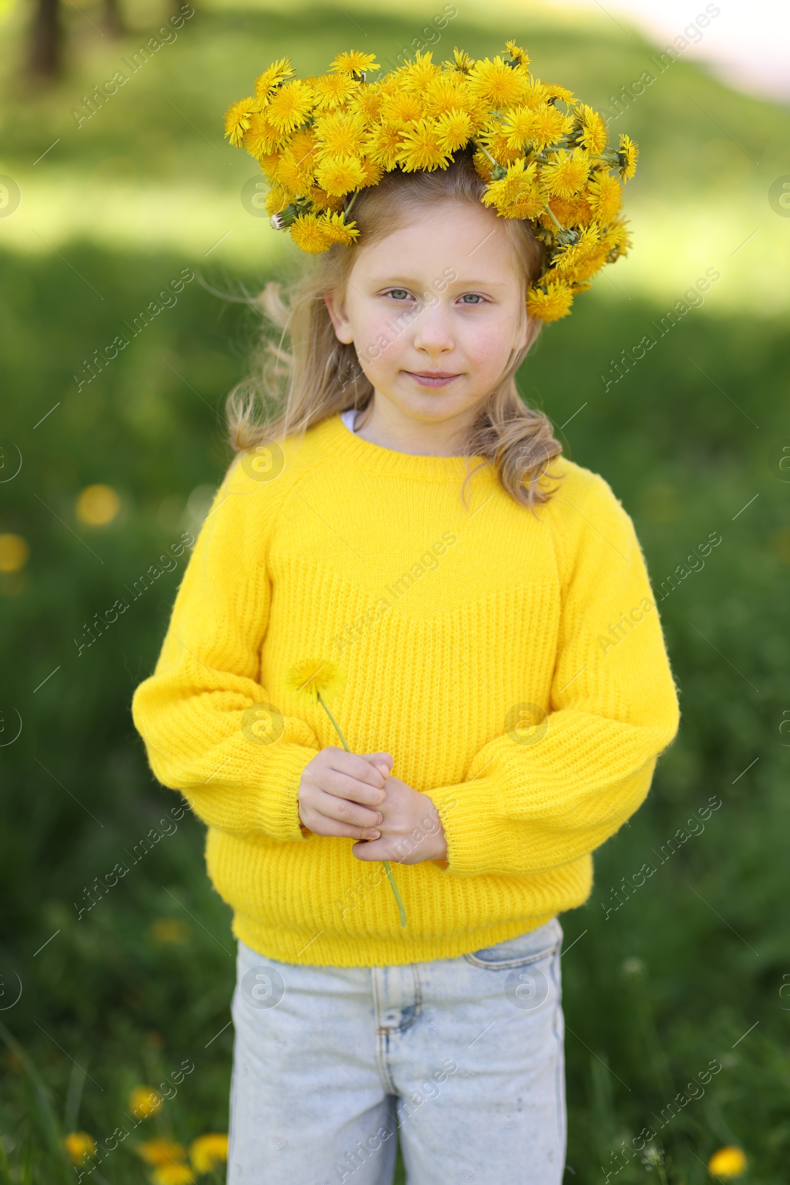 Cute little girl with beautiful flower wearing wreath of dandelions in park Photo of Cute little girl with beautiful flower wearing wreath of dandelions in park