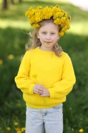 Photo of Cute little girl with beautiful flower wearing wreath of dandelions in park