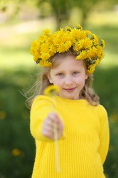 Photo of Cute little girl with beautiful flower wearing wreath of dandelions in park