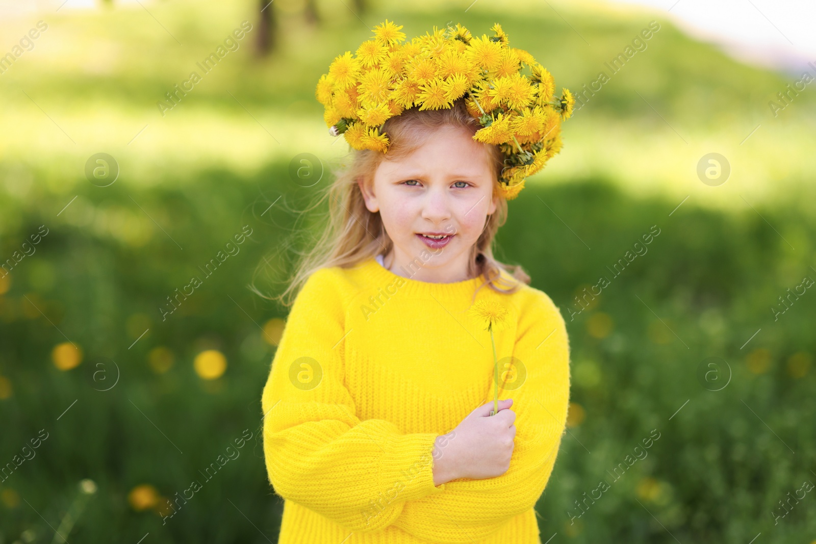 Cute little girl with beautiful flower wearing wreath of dandelions in park Photo of Cute little girl with beautiful flower wearing wreath of dandelions in park