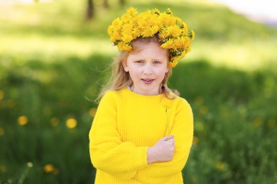 Photo of Cute little girl with beautiful flower wearing wreath of dandelions in park